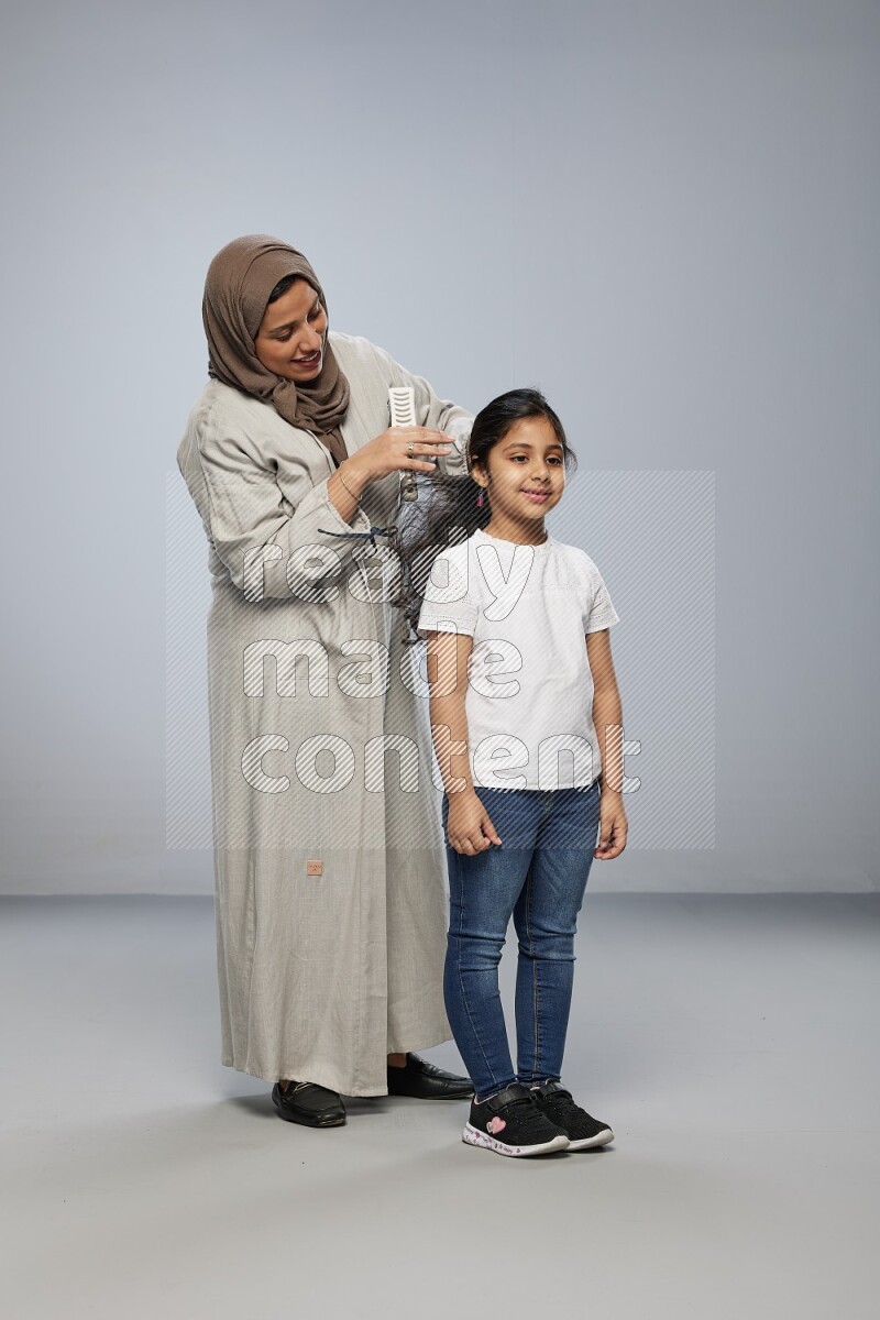 Mom standing styling hair for her daughter on gray background