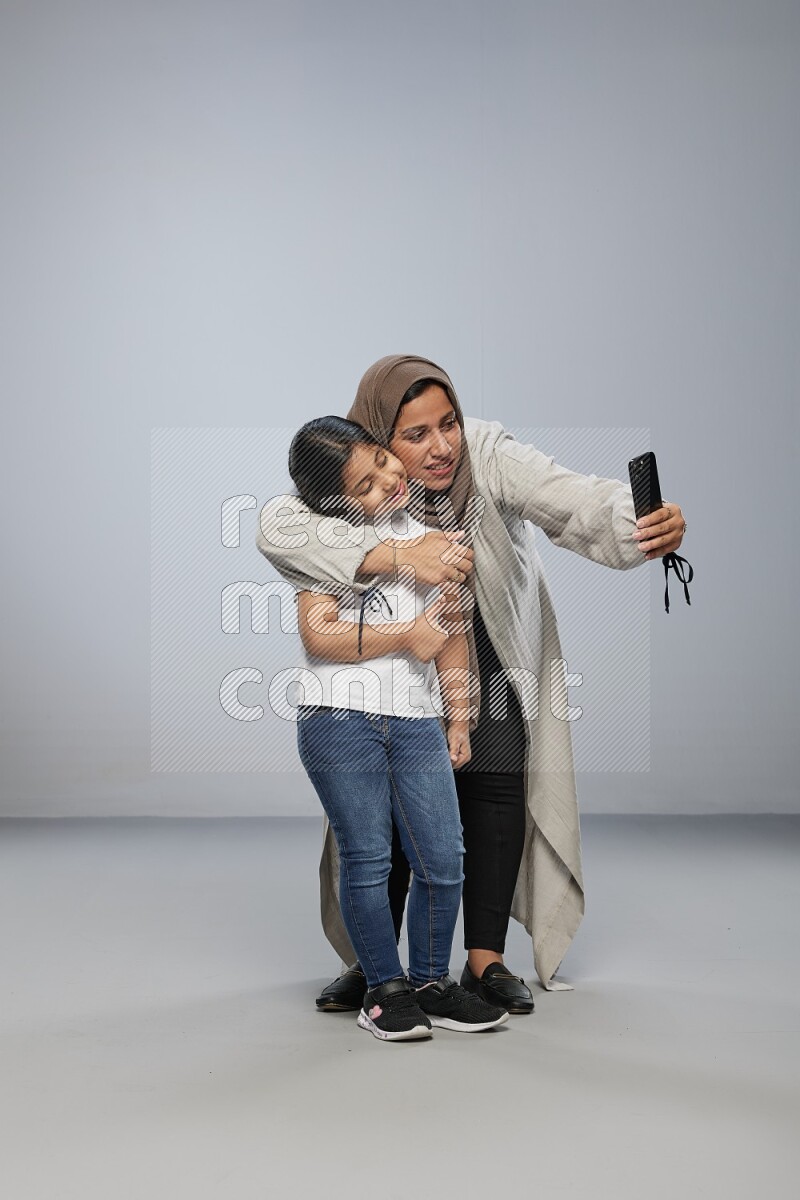 A girl standing taking selfie with her mother on gray background