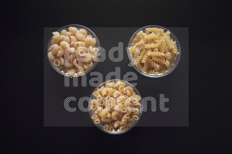 Different pasta types in glass bowls on black background