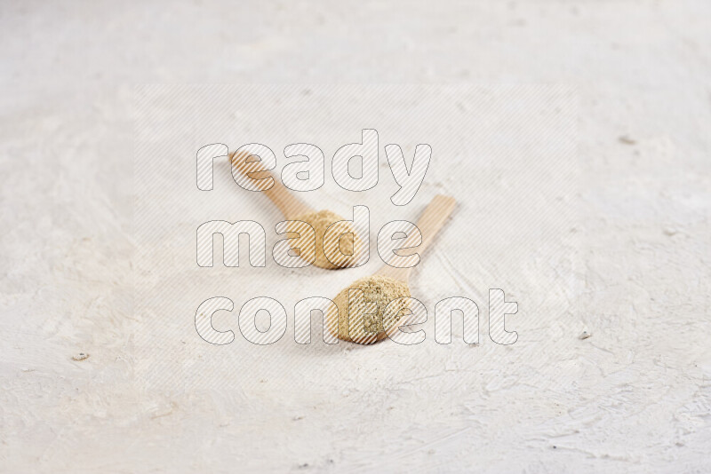Two wooden spoons full of ground ginger powder on white background