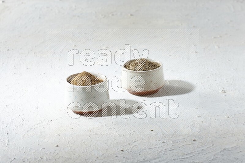2 beige bowls full of cumin seeds and powder on a textured white flooring