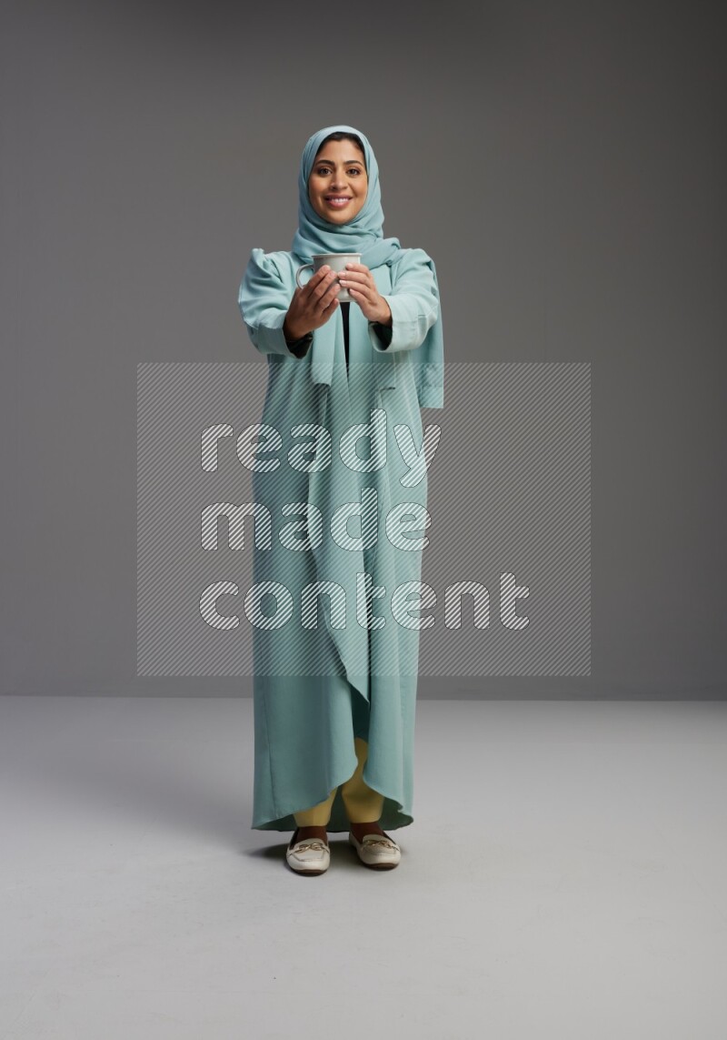 Saudi Woman wearing Abaya standing  holding a mug on Gray background