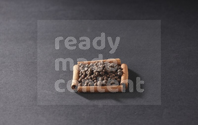 A single square of cinnamon sticks full of allspice on black flooring