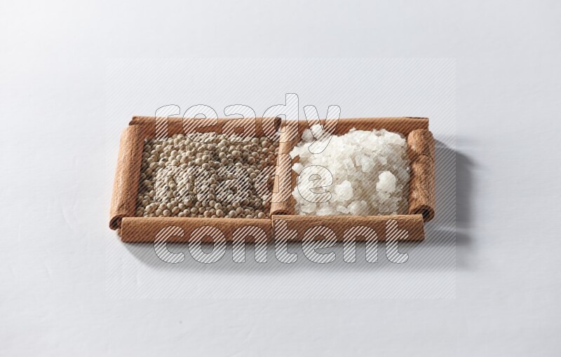 2 squares of cinnamon sticks full of white pepper and white salt on white flooring
