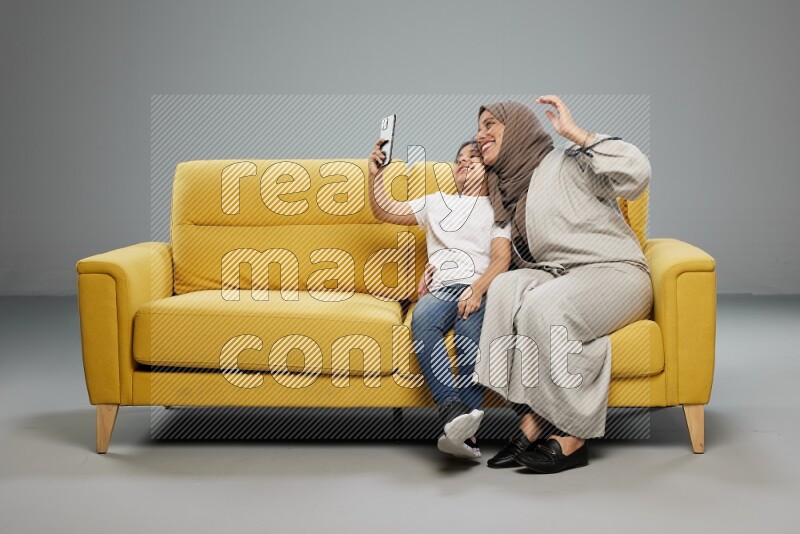A girl sitting taking selfie with her mother on gray background