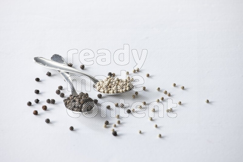 2 metal spoons full of black and white pepper beads with spreaded beads on white flooring