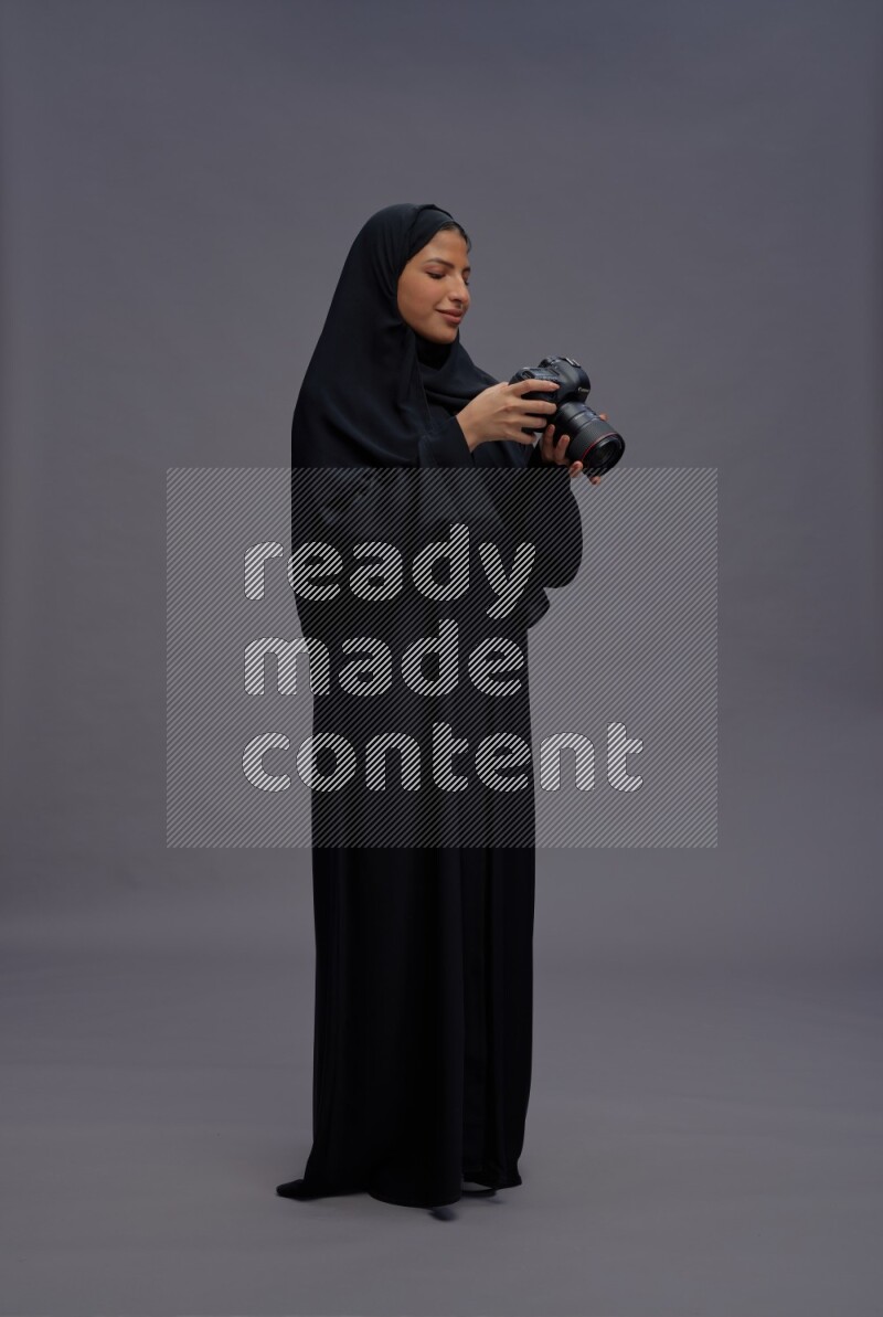 Saudi woman wearing Abaya standing holding Camera on gray background