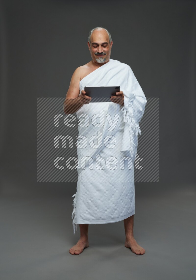 A man wearing Ehram Standing working on tablet on gray background