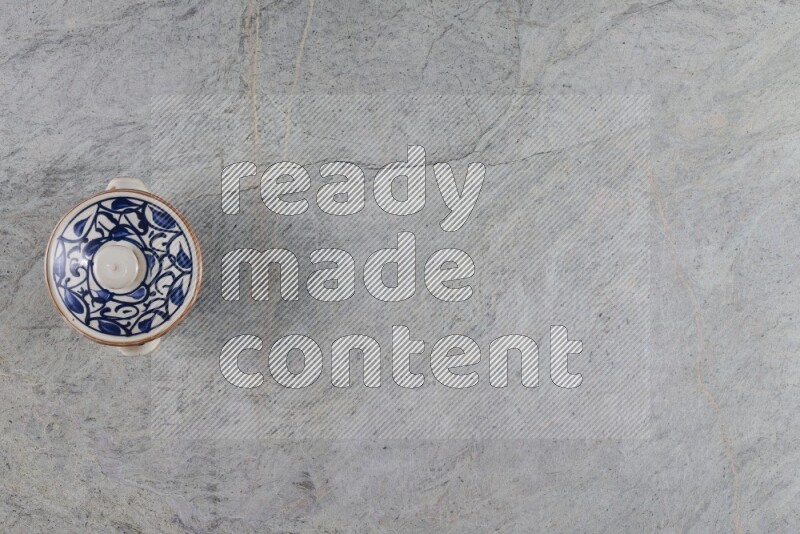 A multicolored pottery pot with its lid on grey marble background