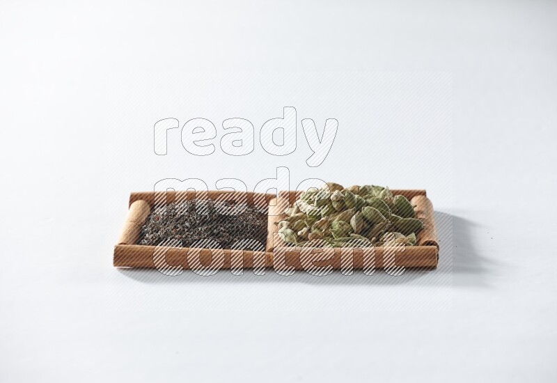 مربعان من أعواد القرفة ممتلئان بالشاي الأسود وحبوب الهال علي خلفية بيضاء