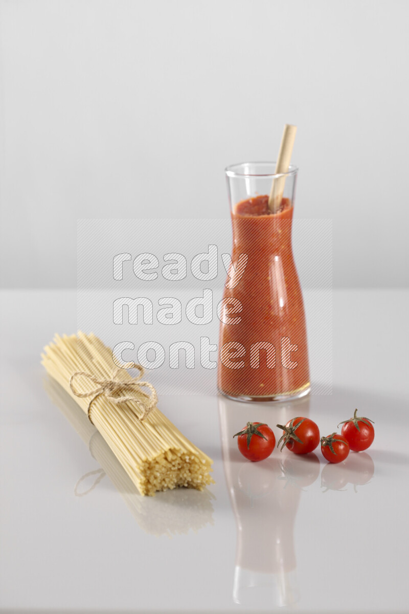 Raw pasta with tomatoe pasta with different ingredients such as cherry tomatoes, basil, garlic, bay laurel, cardamom, white pepper, black pepper, red chilis and wheat stalks on light grey background