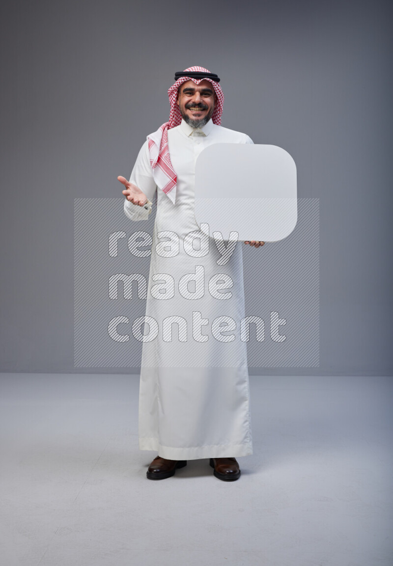 Saudi man Wearing Thob and red Shomag standing holding social media sign on Gray background