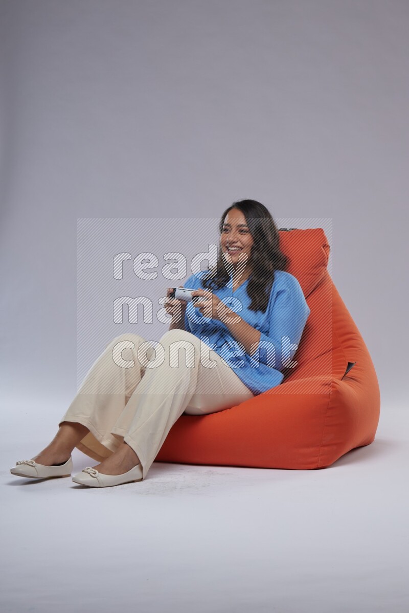 A woman sitting on an orange beanbag and gaming with joystick