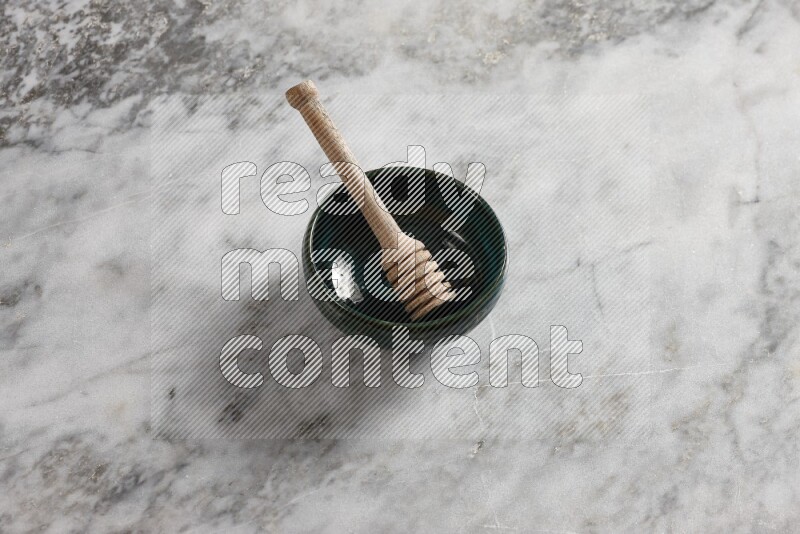 Dark green pottery bowl with wooden honey dipper in it on grey marble background