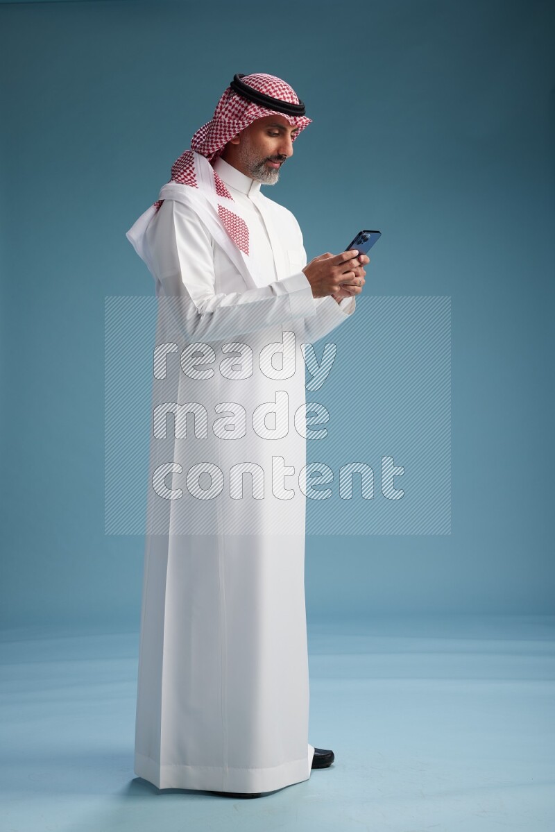 Saudi man wearing thob and shomagh texting on blue background