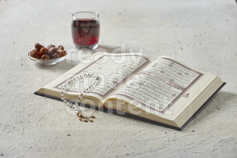 Quran with dates, prayer beads and different drinks all placed on textured white background