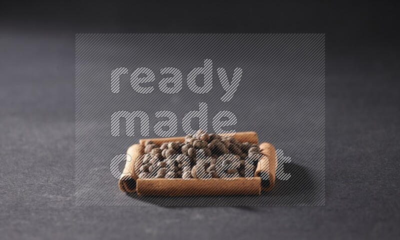 A single square of cinnamon sticks full of allspice on black flooring