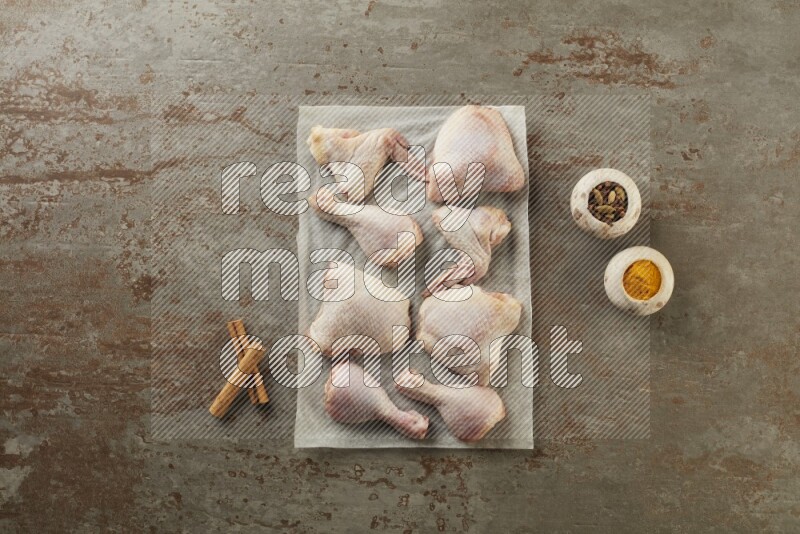Mixed fresh chicken pieces on a parchment paper direct on a textured rustic background