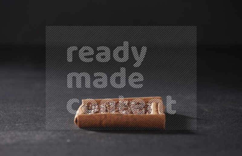 A single square of cinnamon sticks full of flaxseeds on black flooring