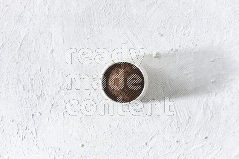 A beige ceramic bowl full of cloves powder on a white flooring