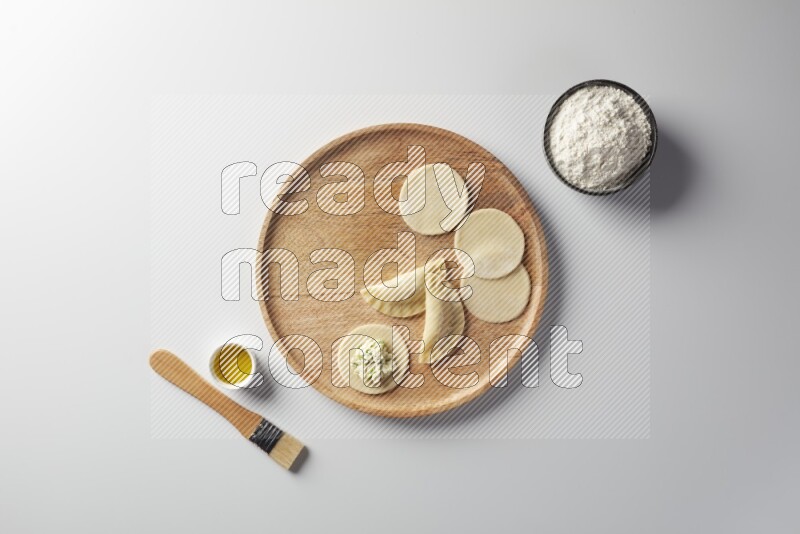 two closed sambosas and one open sambosa filled with cheese while flour, and oil with oil brush aside in a wooden dish on a white background