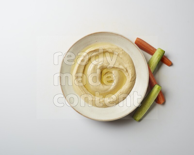 Hummus in a pottry plate garnished with olive oil on a white background