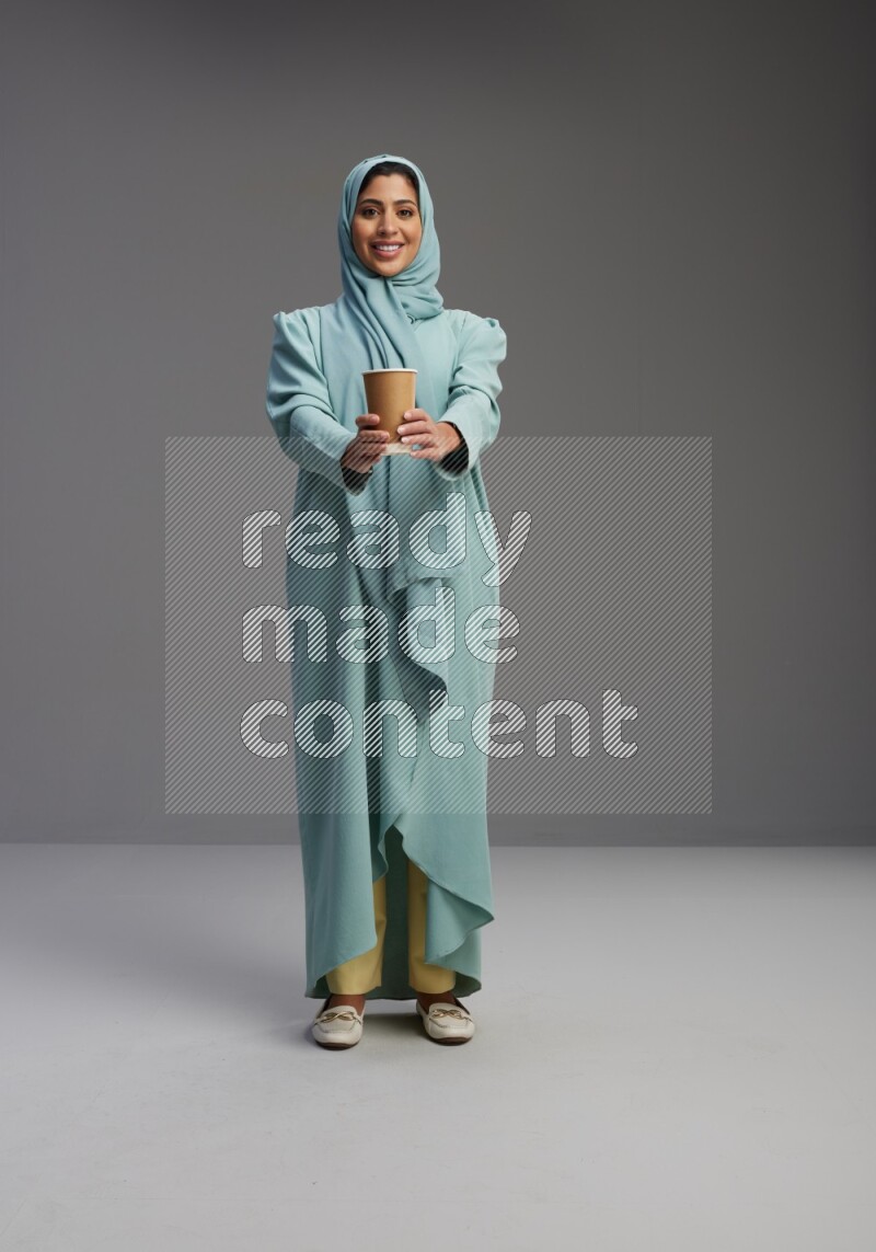 Saudi Woman wearing Abaya standing  holding paper cup on Gray background