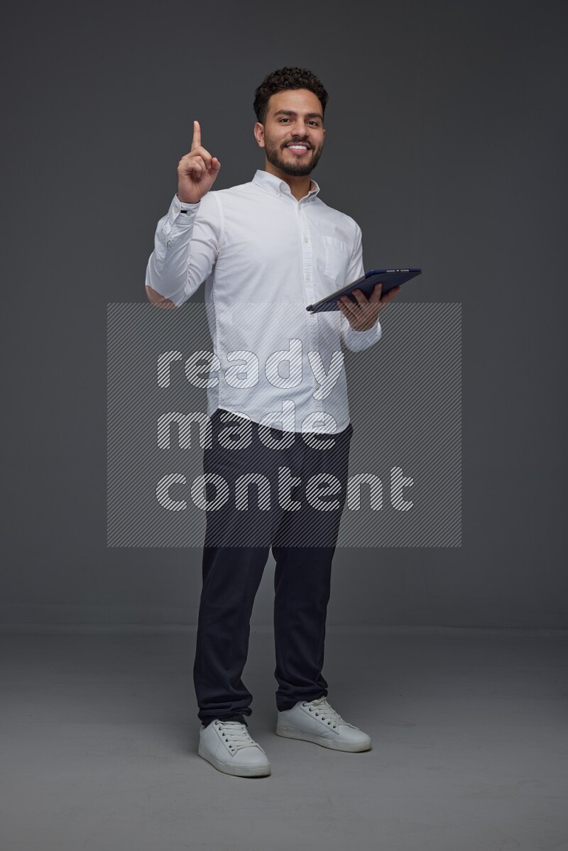 A man wearing smart casual standing and using his tablet and making multi hand gestures eye level on a gray background