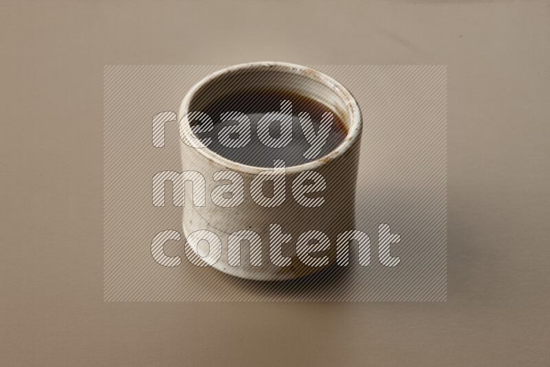 A beige pottery cup of coffee surrounded by roasted coffee beans on beige background
