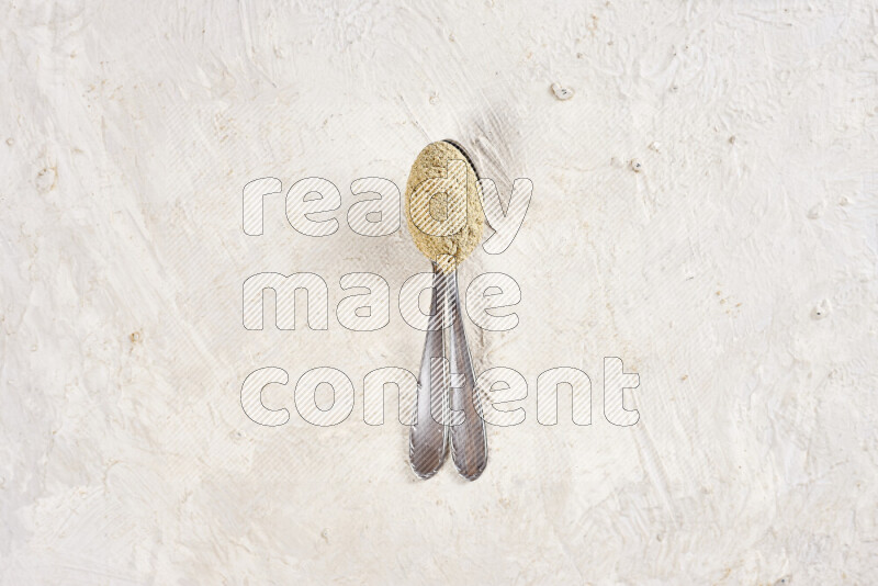 Two metal spoons full of ground ginger powder on white background