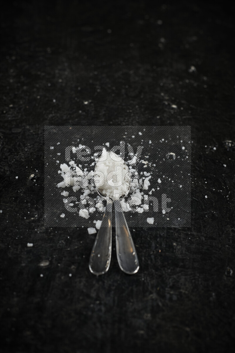 2 metal spoons filled with white salt on black background