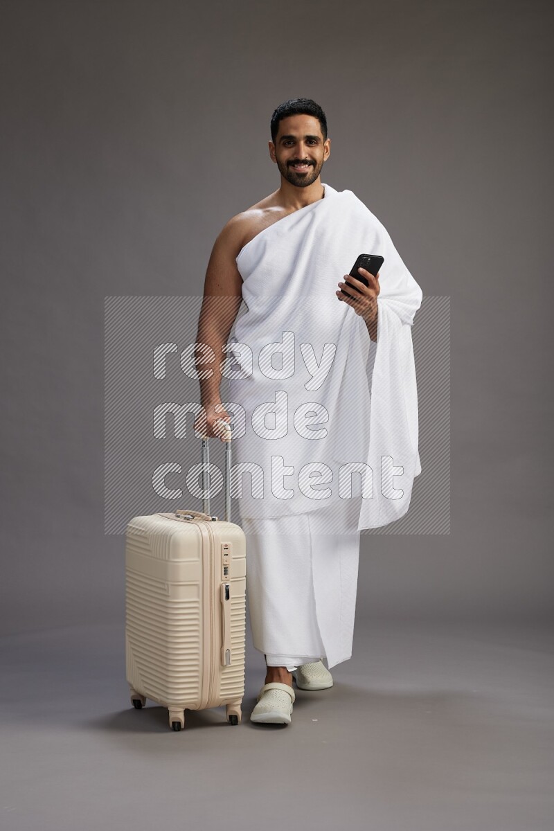 A man wearing Ehram Standing holding traveling bag on gray background