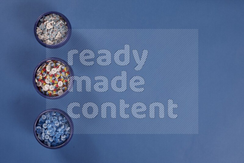 Multicolored pottery bowls full of colored buttons on blue background