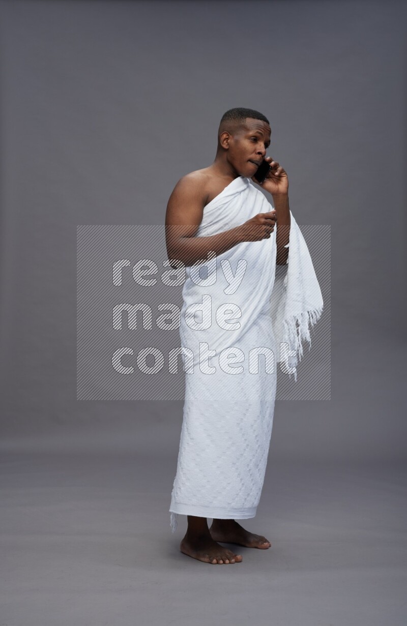 A man wearing Ehram Standing talking on phone on gray background