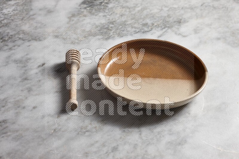 Multicolored pottery oven plate with wooden honey dipper on the side on grey marble background