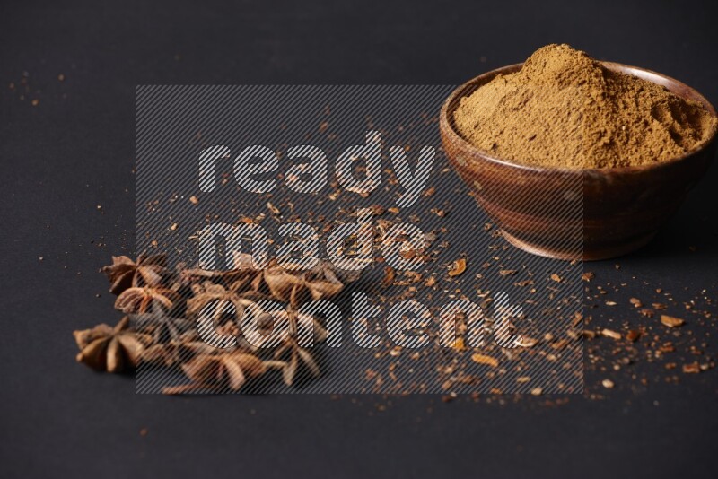 Star Anise powder in a wooden bowl with star anise beside it on a black background