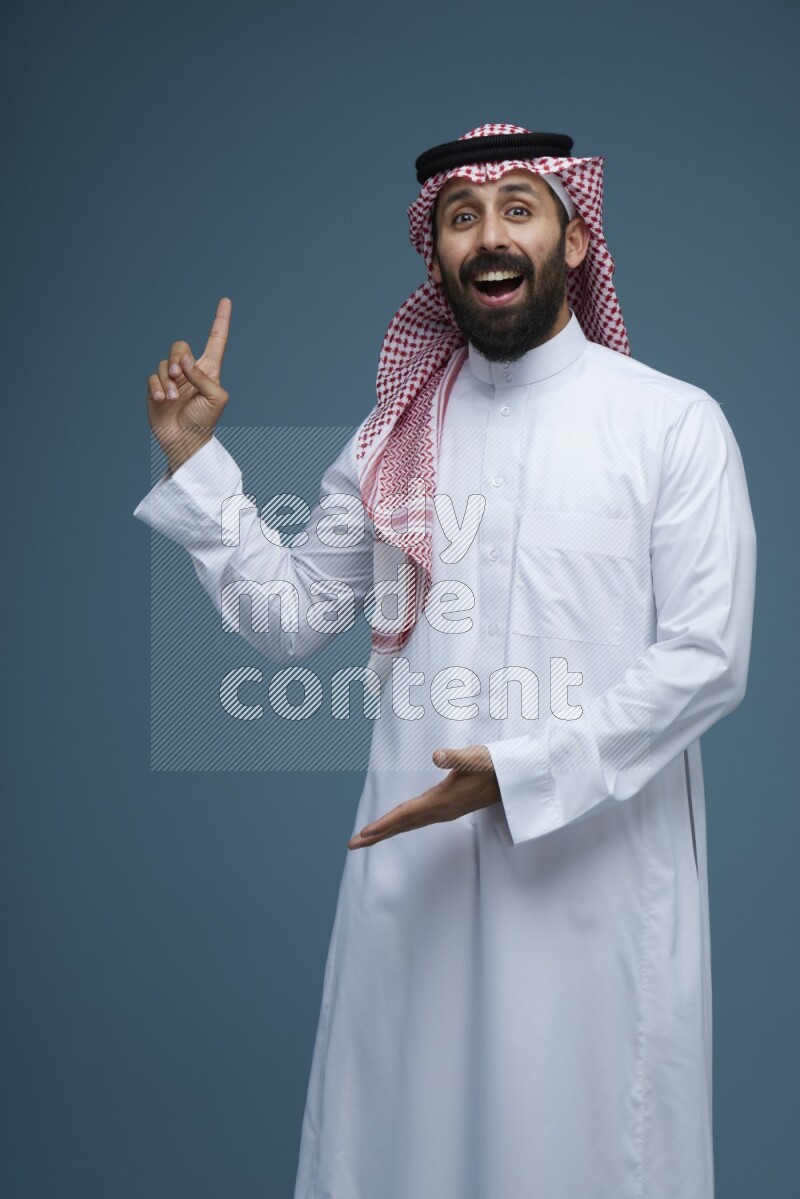 A man pointing in a blue background wearing Saudi Thob and Shomag