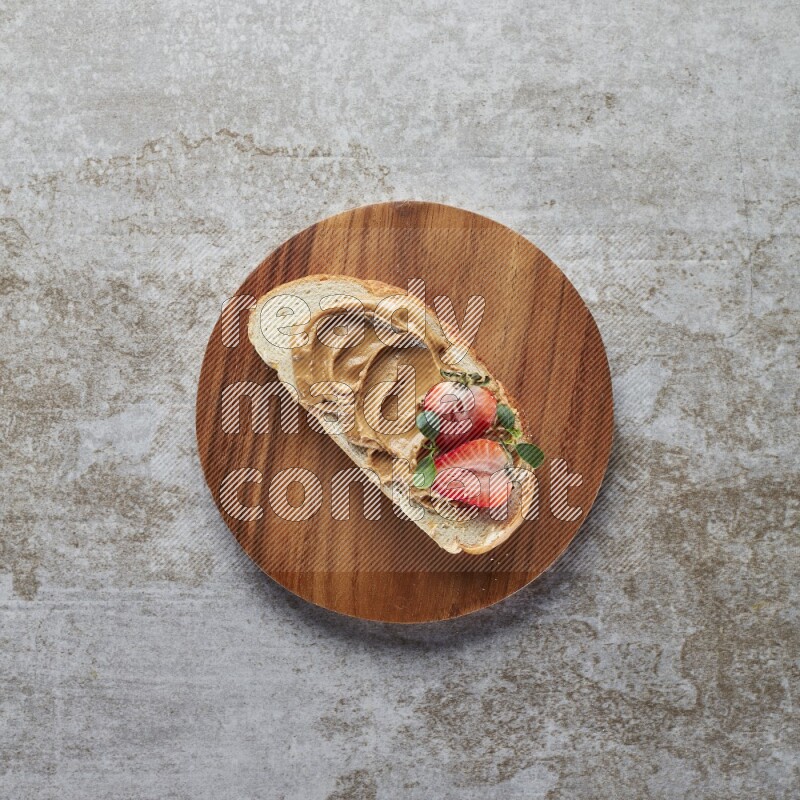 open faced peanut butter sandwich with strawberries on a grey textured background