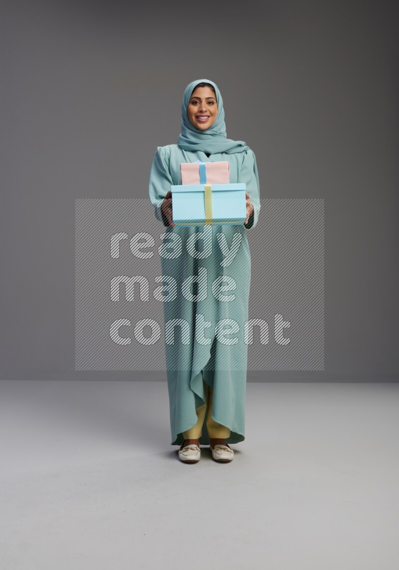Saudi Woman wearing Abaya standing holding gift box on Gray background