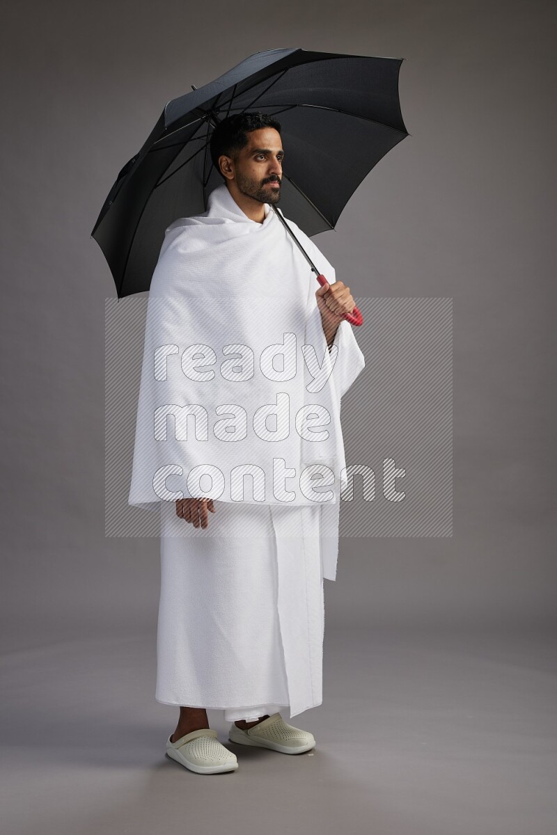 A man wearing Ehram Standing holding umbrella on gray background