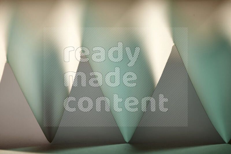 A close-up abstract image showing sharp geometric paper folds in green gradients and warm tones