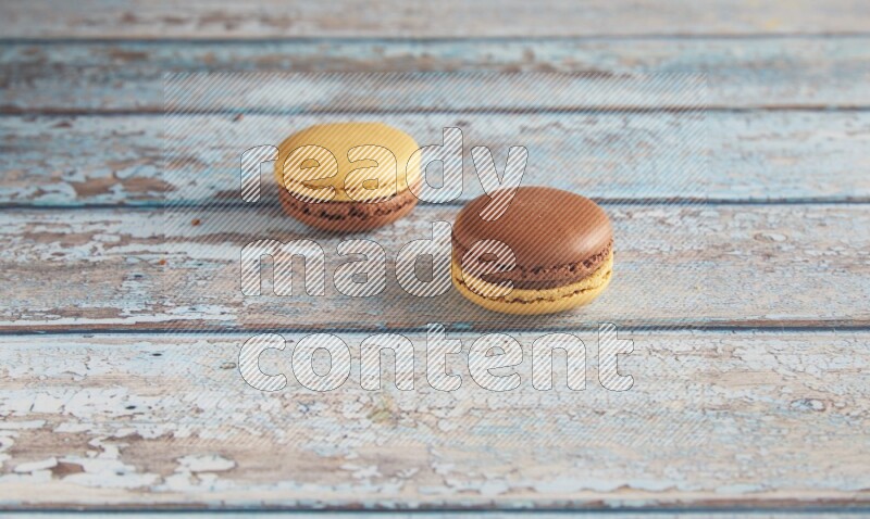 45º Shot of two Yellow and Brown Chai Latte macarons on light blue wooden background