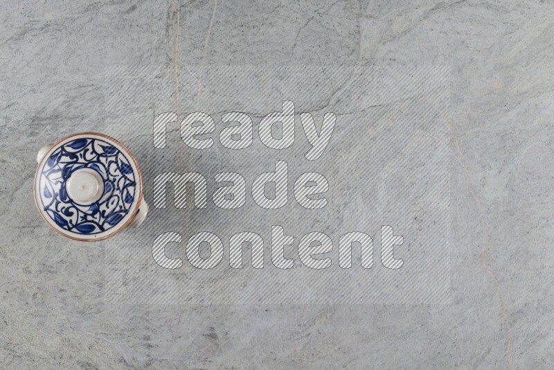 A multicolored pottery pot with its lid on grey marble background
