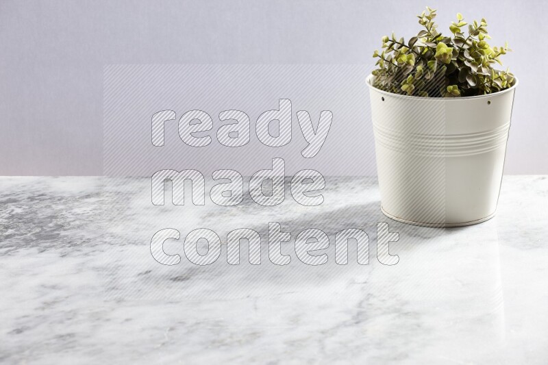 Green artificial plant in white pot on light grey marble background