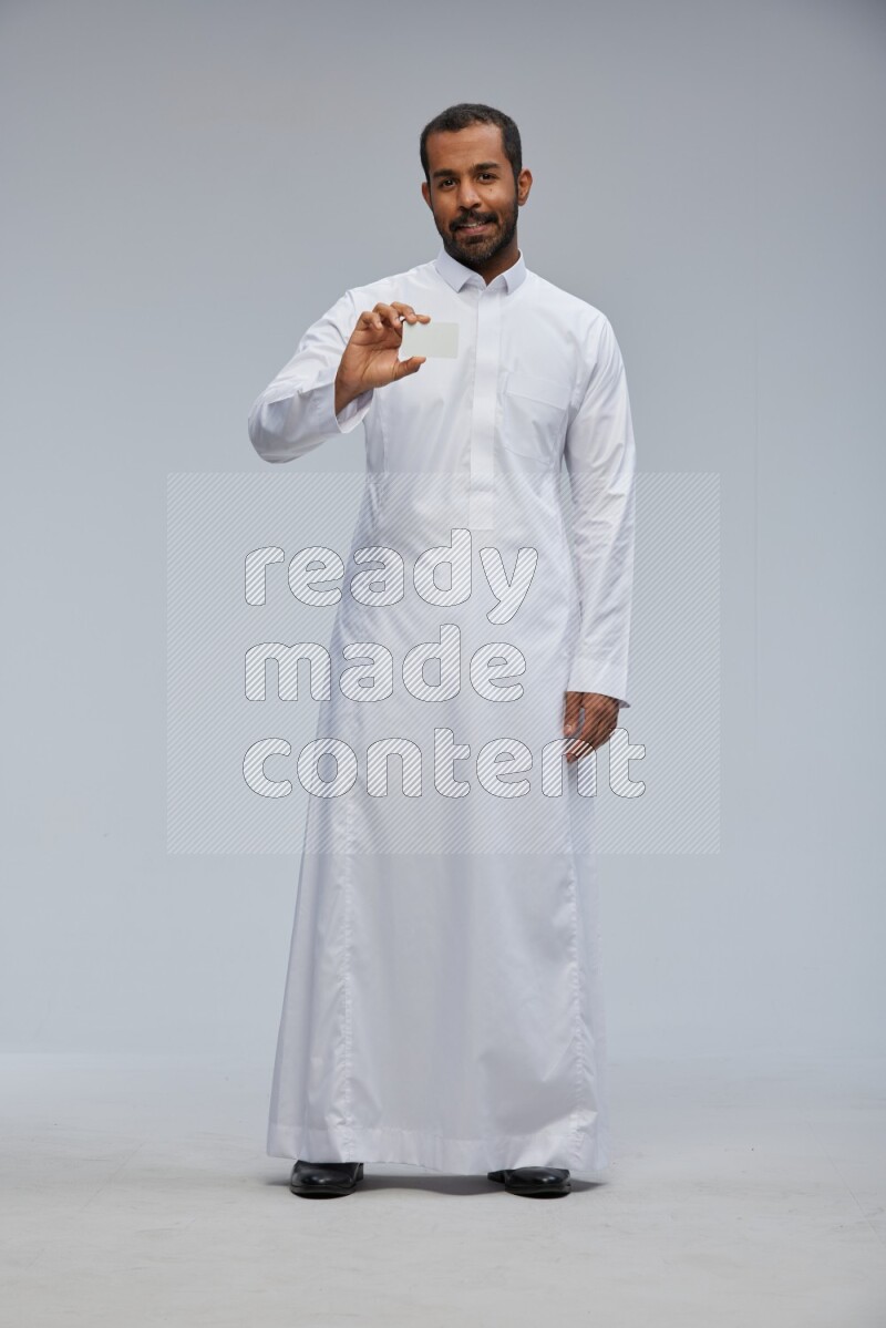 Saudi man wearing Thob standing holding ATM card on Gray background