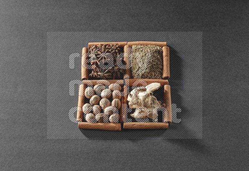 4 مربعات من عيدان القرفة ممتلئة باليانسون النجمي والكمون والزنجبيل المجفف وجوزة الطيب على أرضية سوداء