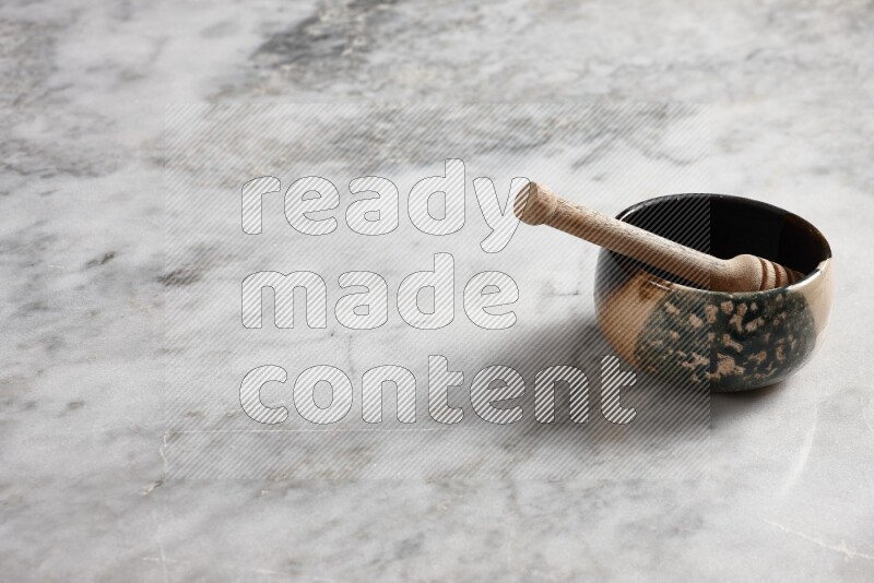 Multicolored pottery bowl with wooden honey dipper in it on grey marble background