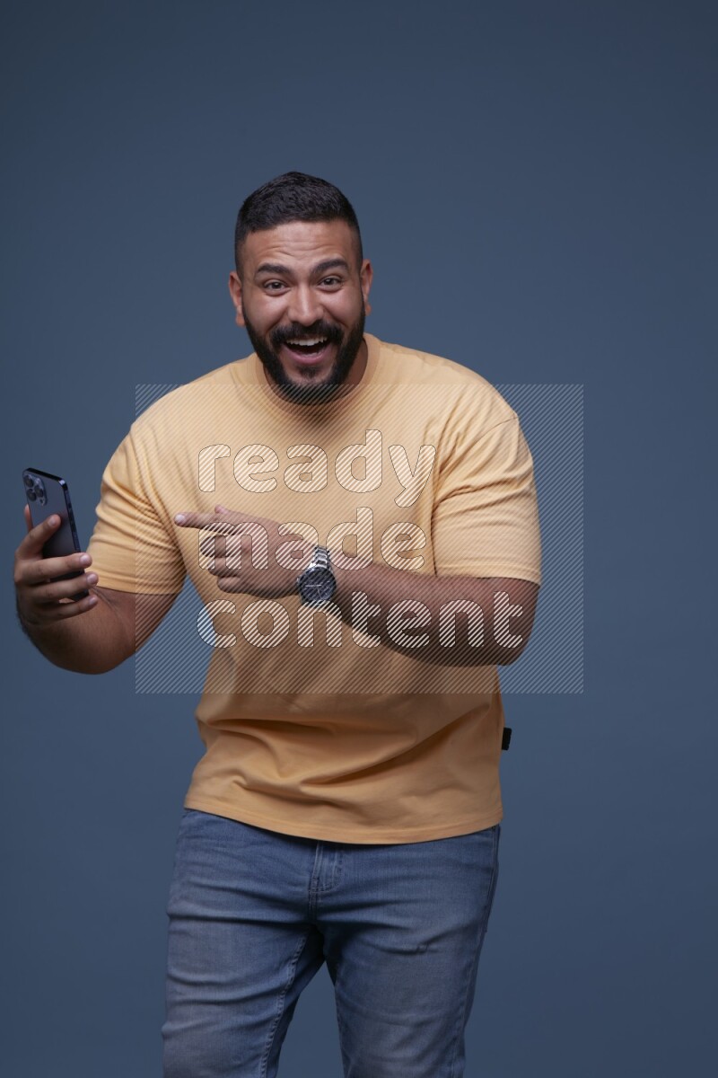 A man Pointing at a Smartphone on Blue Background wearing Orange T-shirt