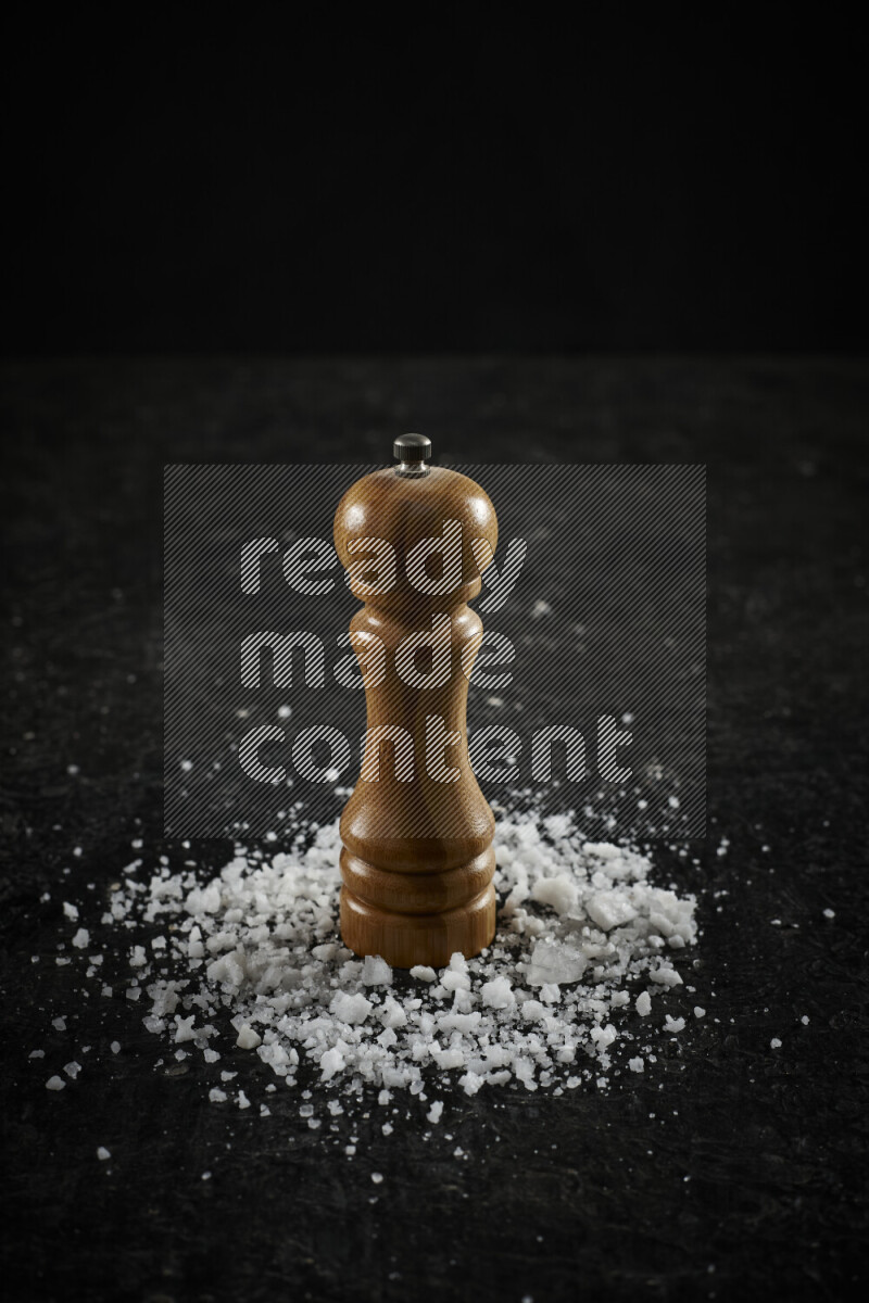 A wooden grinder standing upright and surrounded by coarse white sea salt on black background