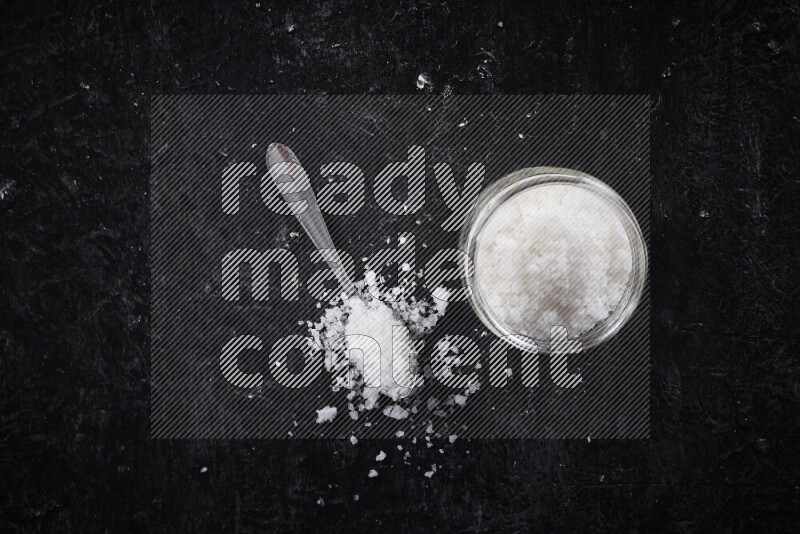 A glass jar full of coarse sea salt crystals on black background